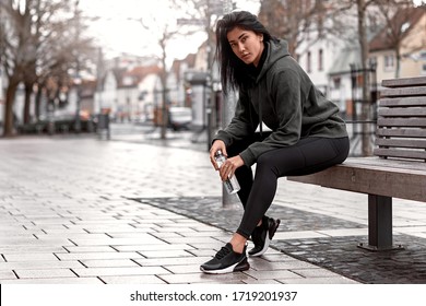 Athletic Women With A Bottle Of Water In Her Hands In A Black Tracksuit Sits On A Bench In The City