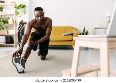 Athletic Young Adult African Man Training And Stretching While Watching Online Fitness Video Tutorial On Laptop Computer At Home - Millennial Guy Doing Workout Routine Following Virtual Gym Class