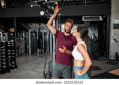 An athletic young adult male coach talking to his female trainee at the gym and showing her the pull-up bars. - Powered by Shutterstock