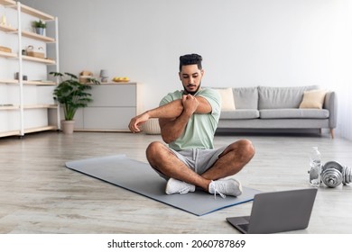 Athletic Young Arab Man Doing Yoga In Front Of Laptop During Home Workout, Copy Space. Attractive Eastern Guy Practicing Pilates, Leading Sporty Lifestyle, Stretching On Mat Indoors, Copy Space