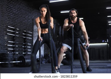 Athletic Young Couple With Battle Rope Doing Exercise In Functional Training Fitness Gym.