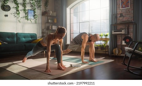 Athletic Young Couple Exercising Together, Stretching And Doing Yoga In The Morning In Sunny Room At Home. Beautiful Man And Woman In Sports Clothes Practising Different Asana Poses On The Mat.