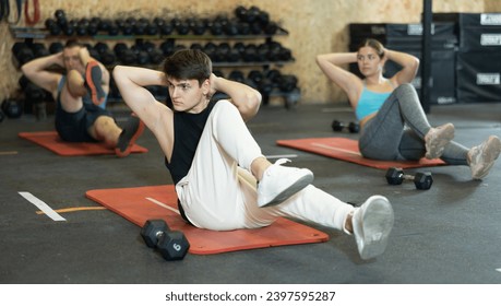 Athletic young guy doing exercises to strengthen abs muscles during group training in gym. Active lifestyle concept