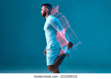 Athletic young guy makes warmup exercise stretching leg in neon studio light. Side view. Long exposure. Fitness club ad - Powered by Shutterstock