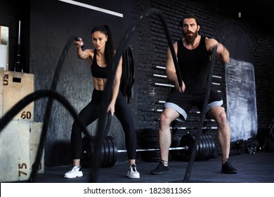 Athletic young indian couple with battle rope doing exercise in functional training fitness gym.