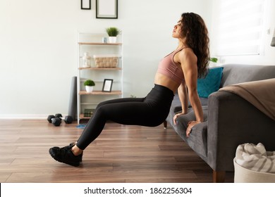 Athletic Young Latin Woman Working Out In Her Home. Woman In Her 20s Doing Tricep Dips Using Her Couch In The Living Room