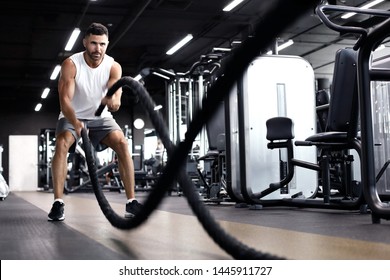 Athletic young man with battle rope doing exercise in functional training fitness gym.