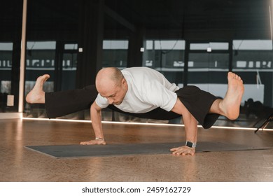 An athletic young man does exercises in the fitness room. A professional guy does yoga in the gym.