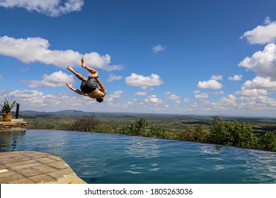 Athletic Young Man Doing Backflip Into Infinity Pool Against Beautiful Blue Sky With Clouds Background During Summertime In Africa