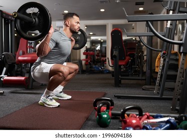 Athletic young man doing barbell squats in the fitness gym - Powered by Shutterstock