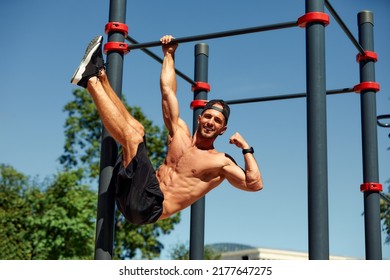 Athletic young man hanging from the bars at the calisthenics gym outdoors smiling - Powered by Shutterstock