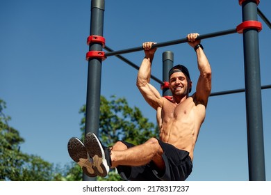 Athletic young man hanging from the bars at the calisthenics gym outdoors smiling