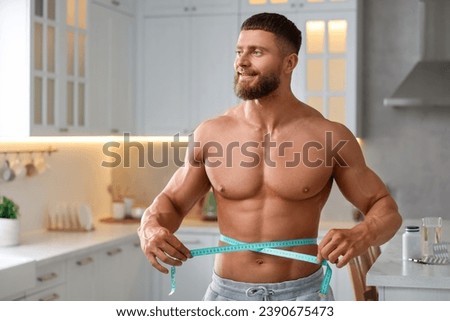 Athletic young man measuring his waist with tape in kitchen, space for text. Weight loss