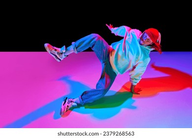 Athletic young man in motion, dancing breakdance isolated over black studio background in neon light. Concept of contemporary dance, street style, fashion, hobby, youth. Ad