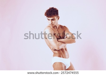 Athletic young man posing confidently in white swimwear against soft pink background, showcasing fitness and body positivity. Personal wellness and health concept.