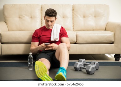 Athletic young man resting and using a smartphone after exercising at home