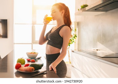 Athletic young red haired woman in the kitchen drinks a glass of fruit centrifuged juice - Shutterstock ID 1942730920
