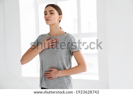 Athletic young sportswoman doing breathing exercise during yoga practice indoors