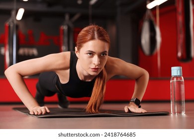 Athletic young woman doing push ups on mat in gym - Powered by Shutterstock