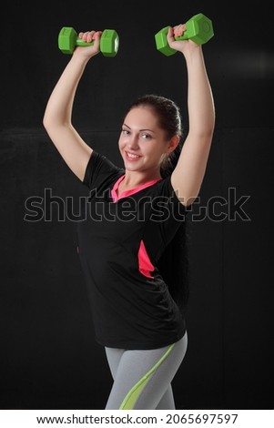 Athletic young woman doing workout with weights on dark background