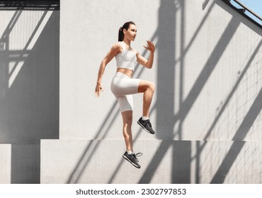 Athletic young woman exercising in the city, do functional training, jumping outdoors. Caucasian female athlete in in sportswear doing fitness workout. Healthy lifestyle concept
