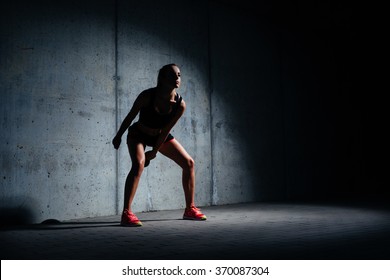 Athletic Young Woman Exercising With Kettlebell In Dark Garage On Concrete Background