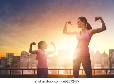 Athletic young woman and her daughter are running on background of urban landscape. Healthy lifestyle. Family sport. 