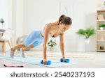 Athletic young woman at home on the floor doing a plank on dumbbells, close-up. Slender girl in sportswear exercising. Concept push ups, sports training, physical exercise, plank workout