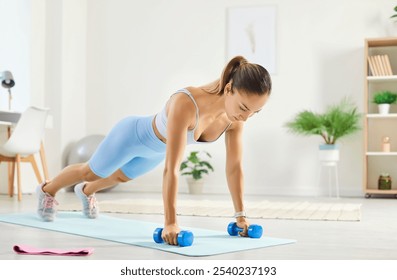 Athletic young woman at home on the floor doing a plank on dumbbells, close-up. Slender girl in sportswear exercising. Concept push ups, sports training, physical exercise, plank workout - Powered by Shutterstock