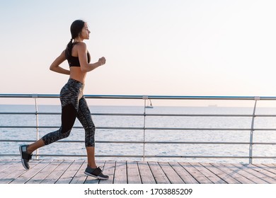 Athletic young woman jogging in the morning by sea wooden embankment. Silhouette of girl in sports costume. Beautiful sunlight. Healthy lifestyle concept. Copy space