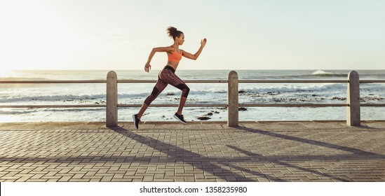 Athletic young woman running on seaside promenade. Side view of female runner sprinting outdoors. - Powered by Shutterstock