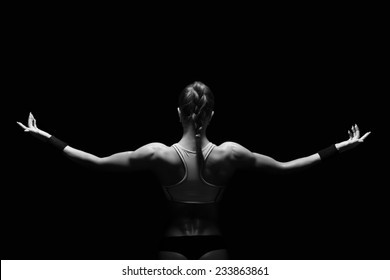 Athletic young woman showing muscles of the back and hands on a isolated black background