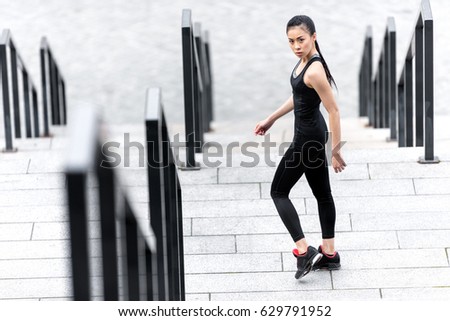 Athletic young woman in sportswear standing on stadium stairs and looking at camera