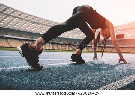Athletic young woman in sportswear in starting position on running track stadium