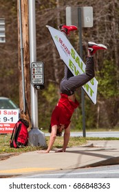 ATLANTA, GA - MARCH 25:  A Young Man Balances A Sign Between His Legs As He Performs A Cartwheel, To Promote A Home Selling Event With Signage On A Street Corner On March 25, 2017 In Atlanta, GA.