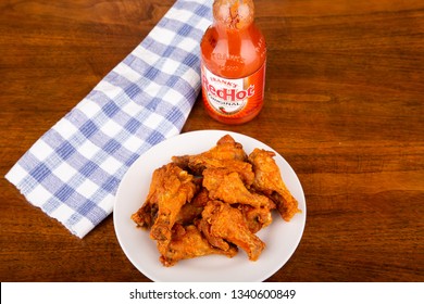 ATLANTA, GEORGIA - April 19, 2017:  Buffalo Chicken Wings On A White Plate With A Bottle Of Frank's Red Hot Sauce In Background