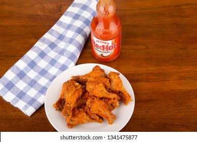 ATLANTA, GEORGIA - April 19, 2017:  Buffalo Chicken Wings On A White Plate With A Bottle Of Frank's Red Hot Sauce In Background