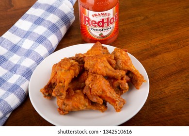 ATLANTA, GEORGIA - April 19, 2017:  Buffalo Chicken Wings On A White Plate With A Bottle Of Frank's Red Hot Sauce In Background