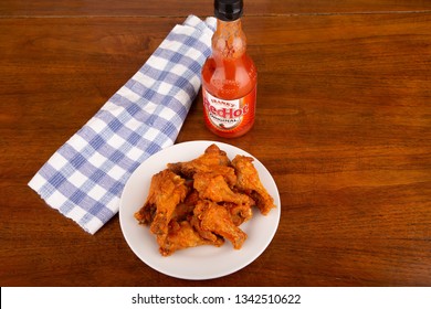 ATLANTA, GEORGIA - April 19, 2017:  Buffalo Chicken Wings On A White Plate With A Bottle Of Frank's Red Hot Sauce In Background