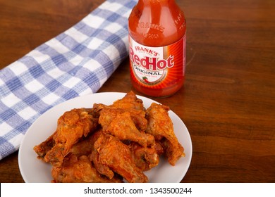 ATLANTA, GEORGIA - April 19, 2017:  Buffalo Chicken Wings On A White Plate With A Bottle Of Frank's Red Hot Sauce In Background