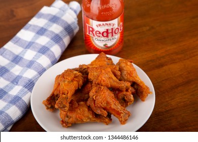 ATLANTA, GEORGIA - April 19, 2017:  Buffalo Chicken Wings On A White Plate With A Bottle Of Frank's Red Hot Sauce In Background