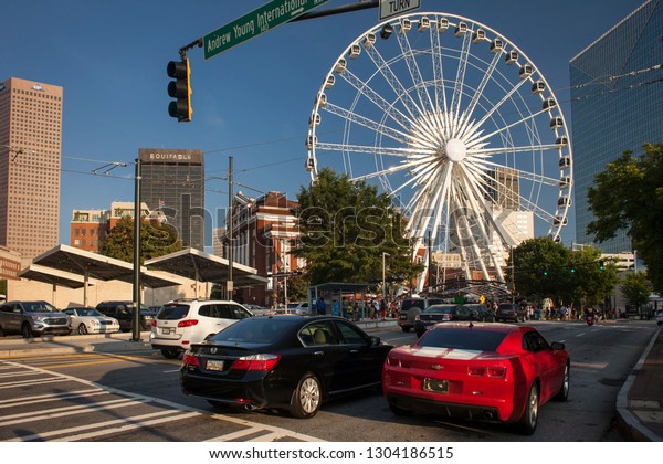 Atlanta, Georgia, USA – July 26, 2015: Horizontal\
shot of the Centennial Olympic Park Dr with two cars at the front,\
one of them a cool sports red car, and the Skyview Atlanta ferris\
wheel at the back
