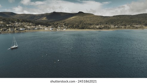 Atlantic ocean gulf, sailboats aerial zooming shot in Brodick Bay. Scottish landscape of port town. Houses, cottages, resort at shore of gulf against greenery lands and mountains view - Powered by Shutterstock