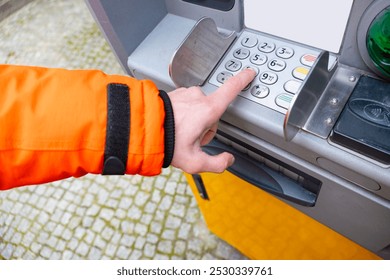 ATM user enters PIN, hand in orange jacket presses button on ATM, importance secure transactions Secure banking transaction at outdoor machine, financial services - Powered by Shutterstock