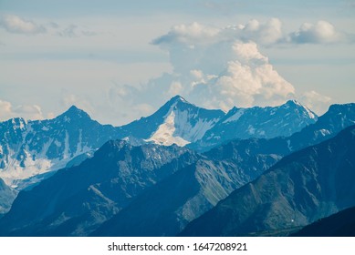 Atmospheric alpine landscape with giant low cloud above great glacier mountain with sunlight on snow. Big rocks and mountains under cloudy sky in sunny day. Awesome minimalist highland scenery.