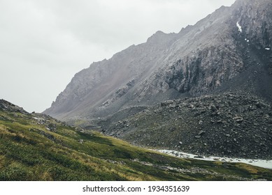 Atmospheric alpine landscape with narrow valley with mountain creek and sharp rocks under gray sky. Bleak highlands scenery with pointed rockies on mountainside and mountain creek in overcast weather.