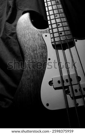 An atmospheric black and white photograph of a bass guitar with an emphasis on the details of the body and strings. The artistic play of light and shadow highlights the texture of the instrument, crea