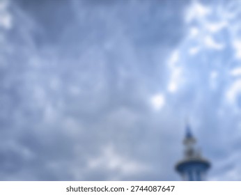 An atmospheric and blurry image capturing a cloudy blue sky with a softly focused, indistinct architectural spire.