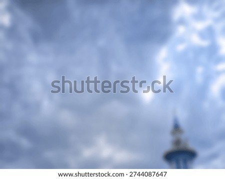 An atmospheric and blurry image capturing a cloudy blue sky with a softly focused, indistinct architectural spire.