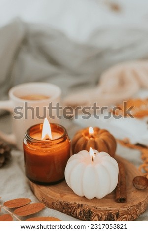Atmospheric candles - shape of pumpkins and candle in amber glass jar with wooden wick, autumn decor on gray bed. Autumn cozy home and hygge concept